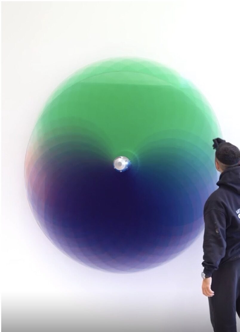 A visitor standing before a large circular gradient work by Felipe Pantone, shading from green into deep blue.